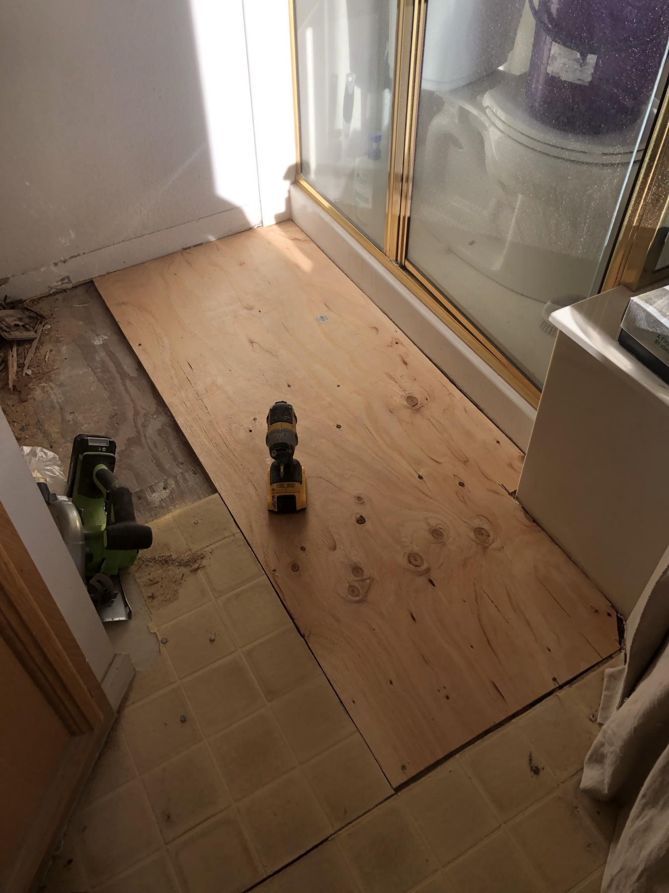 New plywood subfloor installed in a bathroom beside the shower