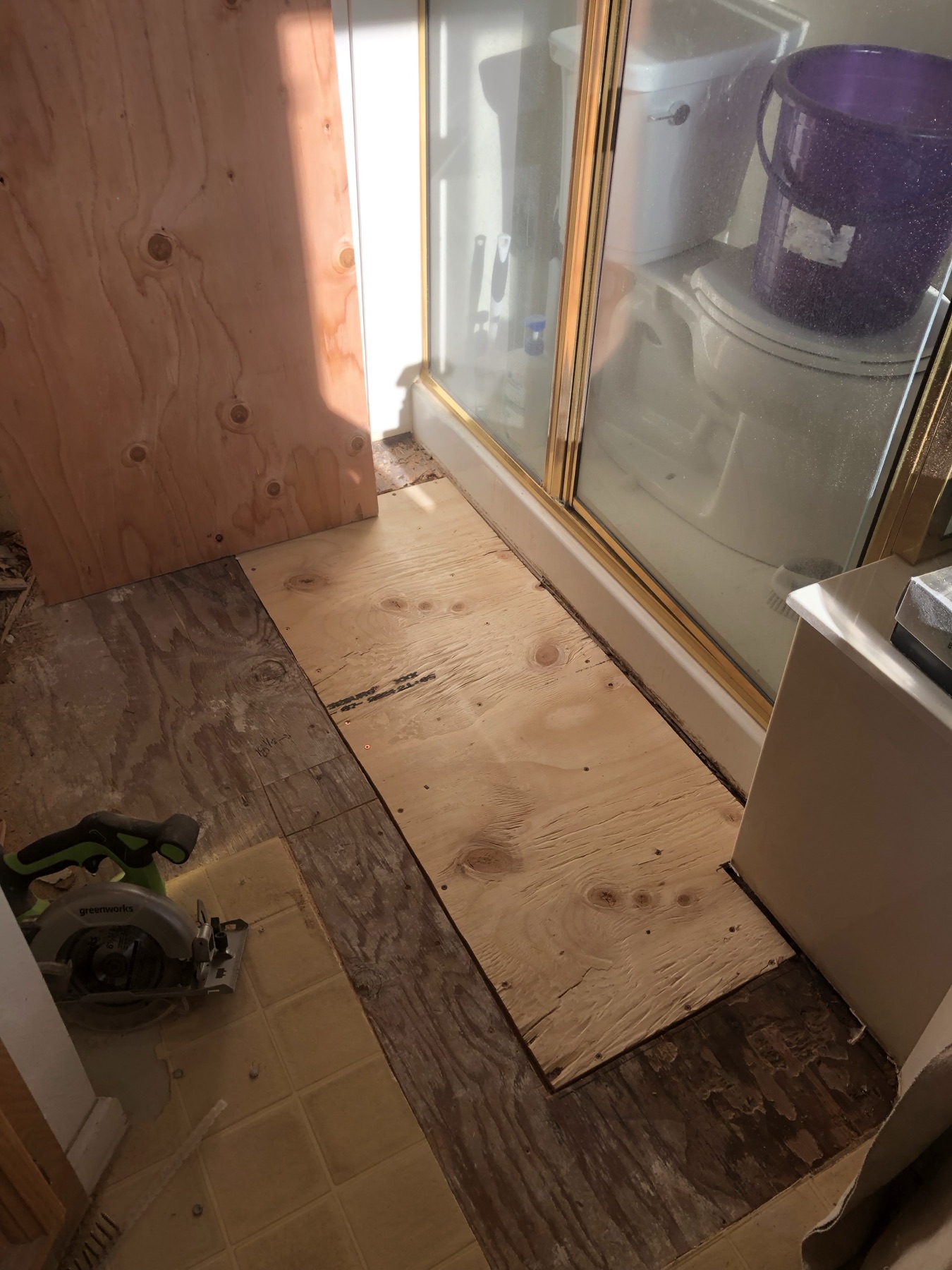 Plywood subfloor and old vinyl flooring next to a shower during a floor rebuild
