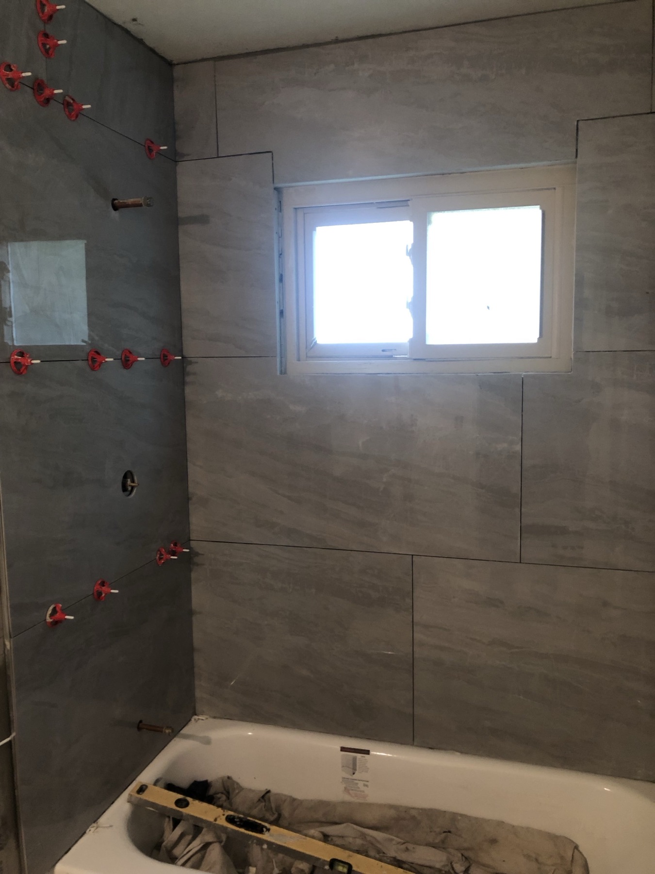 Large gray wall tile being set around a bathtub and window during a bathroom remodel