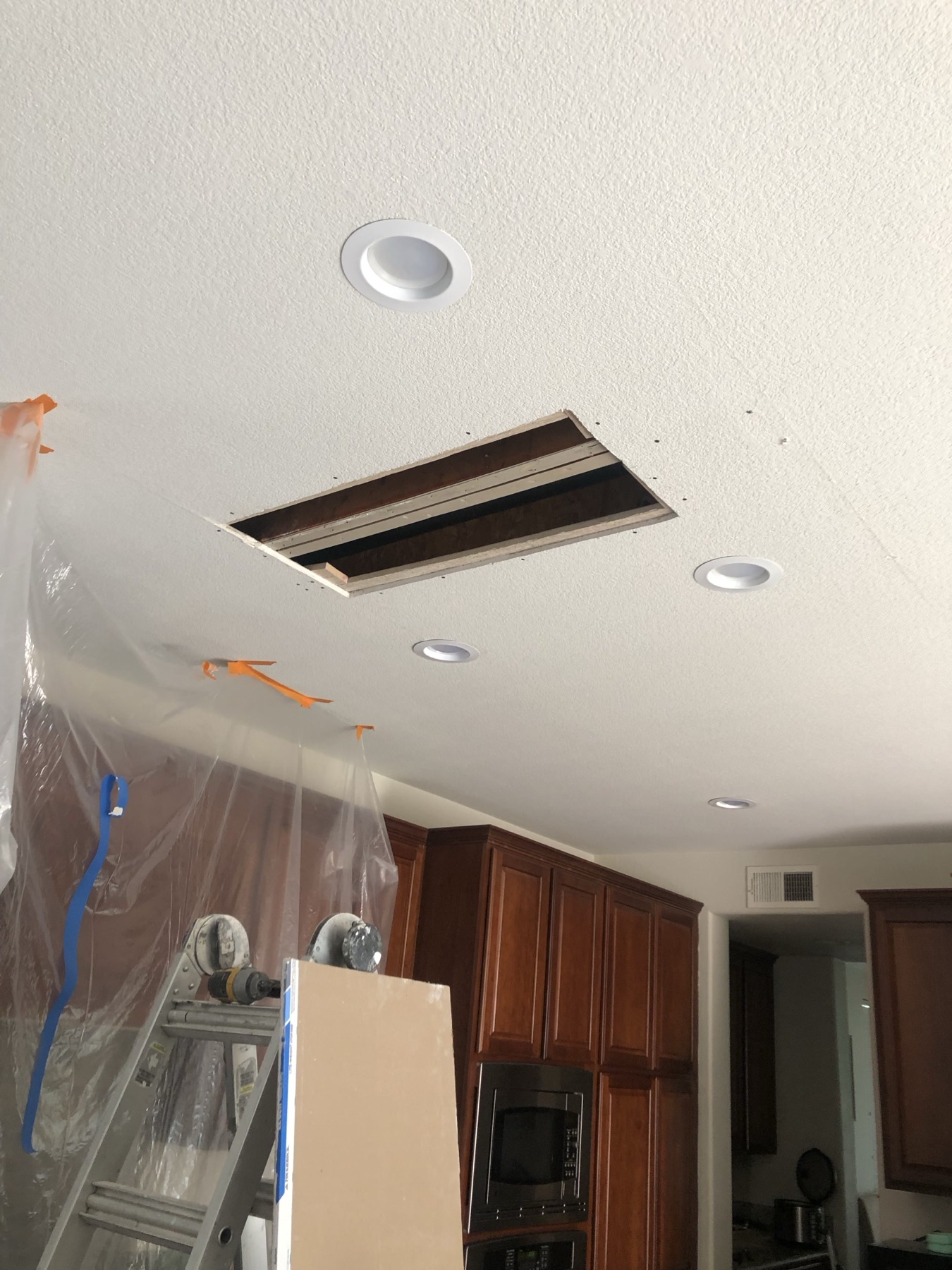 Kitchen ceiling opened up for repair, with the cabinets protected under plastic sheeting