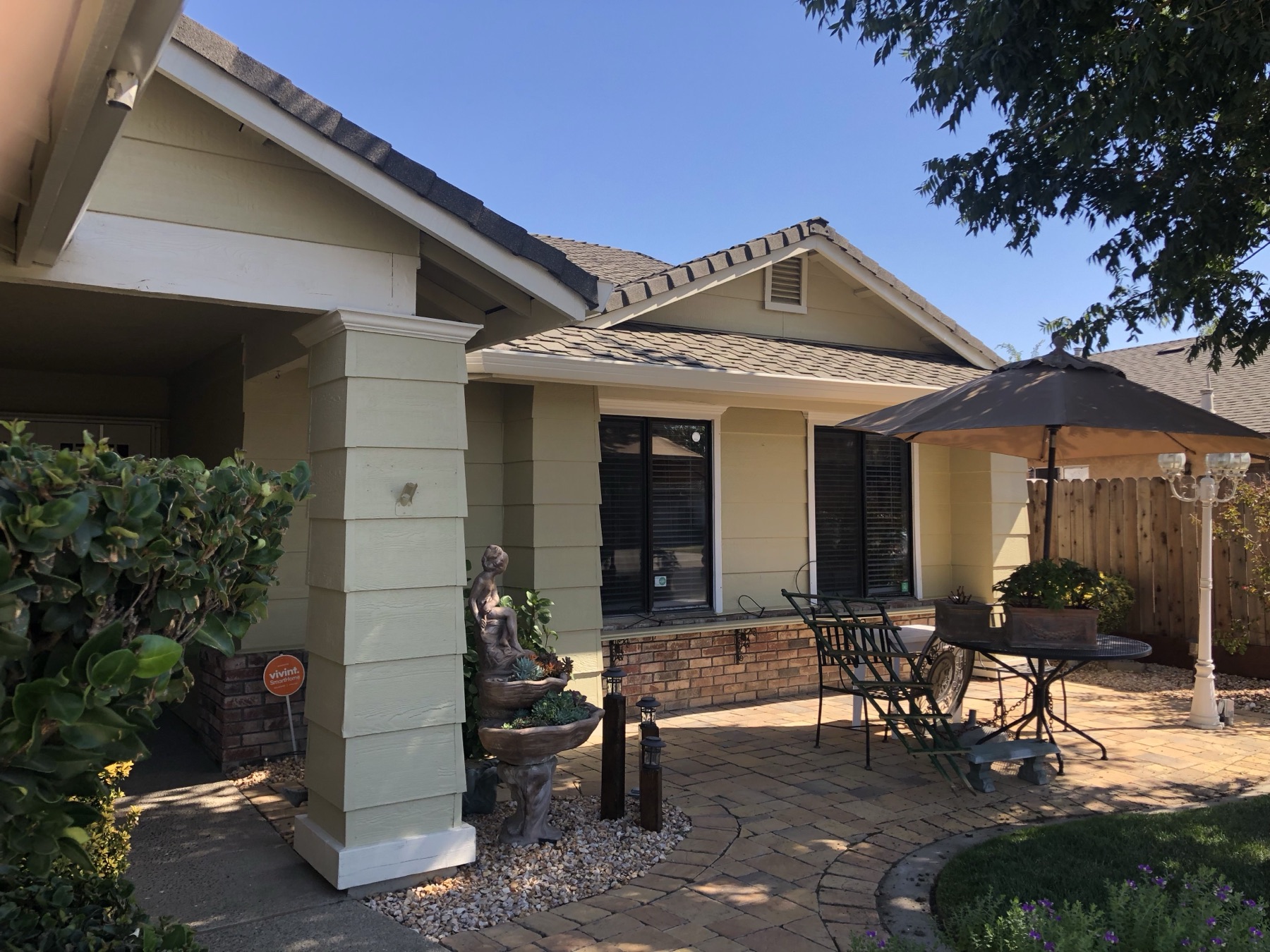 Freshly painted sage green home with cream trim beside a covered patio