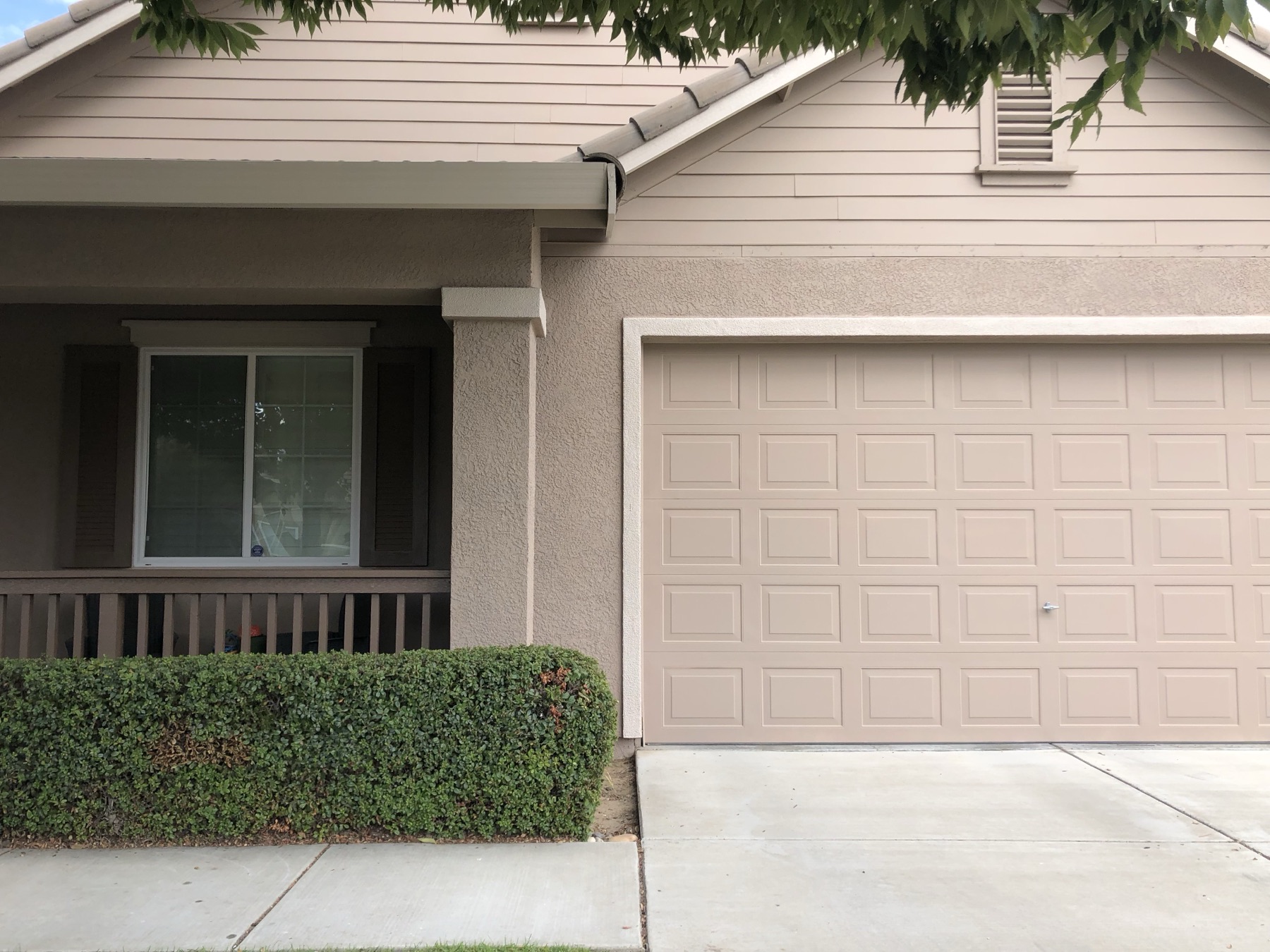 Front of a repainted tan home showing the garage door, porch and window trim